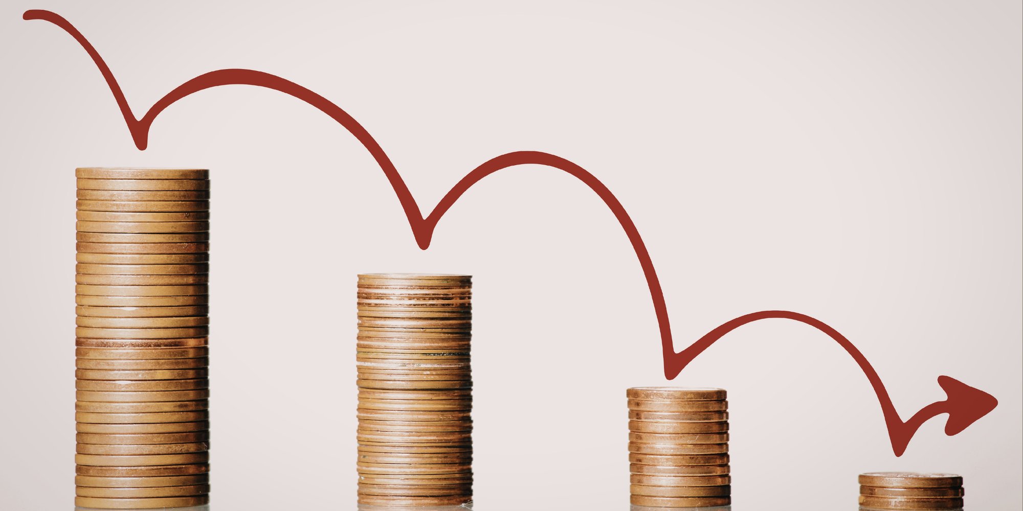 Four stacks of coins decreasing in height from left to right, with a red line graph showing a downward trend and an arrow pointing right.