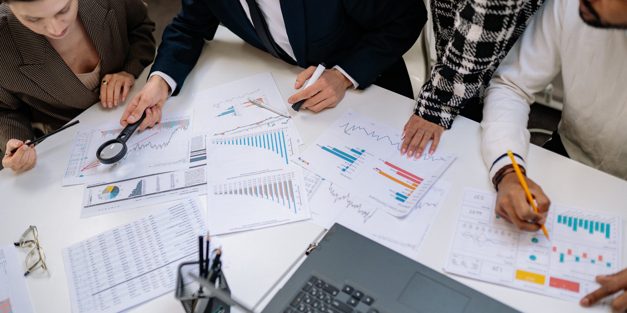 A group of people gathered around a table, analyzing charts and graphs with a magnifying glass and pens.